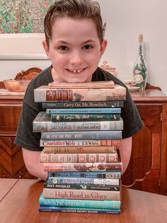 a young boy sitting at a table with a stack of books in front of him