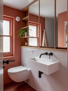 a white toilet sitting next to a bathroom sink under a mirror on top of a wall