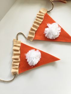 two pieces of felt with white pom poms on top of each other, hanging from twine strings