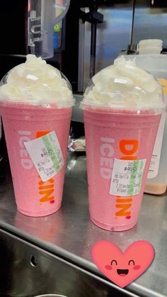 two pink cups with whipped cream on top sitting on a metal counter next to each other