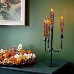 an arrangement of candles on a table in front of a painting and bowl of flowers