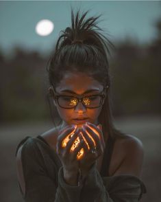 a woman wearing glasses and holding her hands in front of her face with the moon behind her