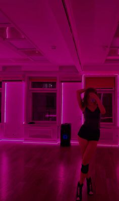 a woman standing in a room with pink lights on the walls and floor, wearing short shorts