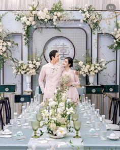 a man and woman standing next to each other in front of a table with flowers