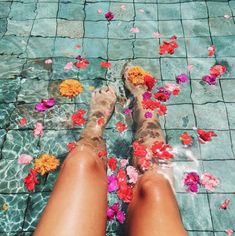 a woman's legs in water with flowers floating on the ground next to them