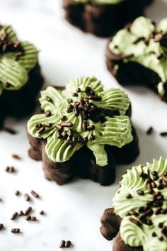 chocolate cookies decorated with green frosting and sprinkles on a white surface