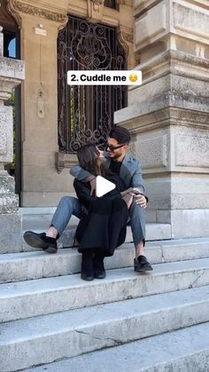 a man and woman sitting on the steps in front of a building with their faces close to each other