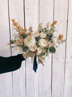 a woman holding a bouquet of flowers in front of a wooden wall with white boards