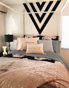 a bed with black and white sheets, pink pillows and a decorative headboard on the wall