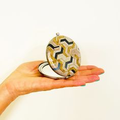 a woman's hand holding a compact mirror with gold and black designs on it