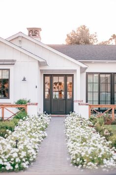 a white house with black doors and flowers in the front yard on a sunny day