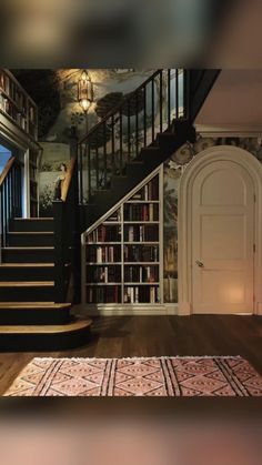 a room with stairs, bookshelves and rugs on the wooden flooring