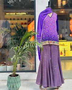 a mannequin dressed in purple stands next to a potted plant