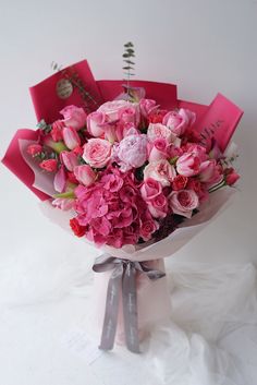 a bouquet of pink flowers is wrapped in red paper and tied to a ribbon on a white surface