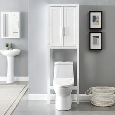 a white toilet sitting in a bathroom next to a tall cabinet and sink with pictures on the wall