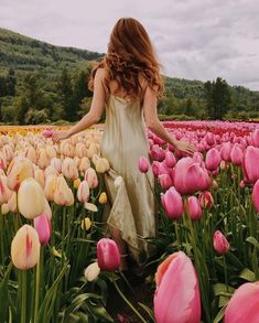 a woman walking through a field full of pink and yellow tulips with her hands in the air