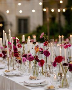 the table is set with candles and flowers in vases, plates and napkins