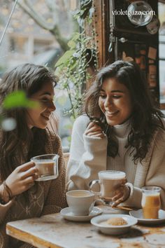 two women sitting at a table with cups of coffee in front of them and smiling