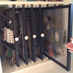 a person is holding up a display case with many necklaces and rings on it