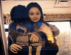 two women hugging each other on a bus in front of a window with the reflection of another woman