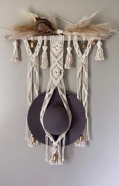 a hat hanging on the wall next to a macrame with feathers and tassels