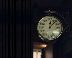 a clock hanging from the side of a building with words on it's face