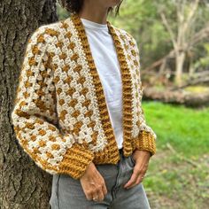 a woman standing next to a tree wearing a crocheted jacket