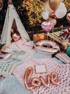 a table topped with lots of pink and gold balloons next to a teepee tent