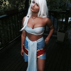 a woman with white hair wearing a blue and red outfit standing on a wooden deck