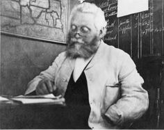 an old black and white photo of a man sitting at a desk with a book