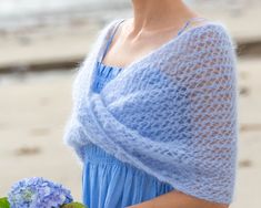 a woman in a blue dress holding a bouquet of flowers and wearing a knitted shawl