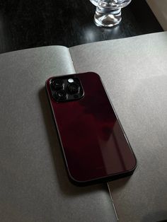 a red cell phone sitting on top of a table next to a glass vase filled with water