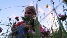 a woman is standing in the tall grass and talking on her cell phone while holding flowers