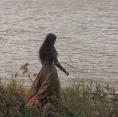 a woman in a long dress standing by the water