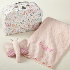 a pink blanket, mittens and suitcase on a white surface