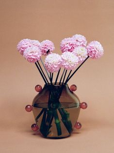 pink carnations in a green vase on a brown background with pearls around the stems