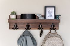 a wooden shelf with hooks and two coats hanging from it's sides next to a backpack