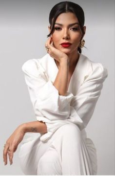 a woman sitting on top of a white chair with her hand under her chin and looking at the camera