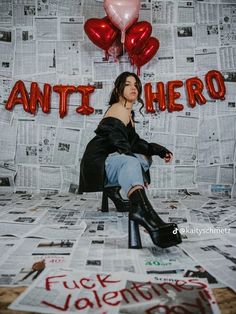 a woman sitting on a chair in front of a wall with red and pink balloons