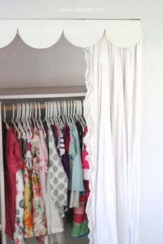 an open closet with clothes hanging on hangers and white drapes over the door