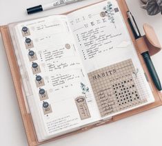 an open planner book sitting on top of a desk next to a pen and plant