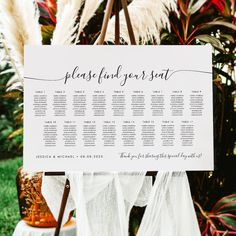 a seating chart on a easel in front of some plants and flowers at a wedding