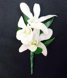 a white flower with green leaves is on a black tablecloth and it appears to be in the shape of a bouquet