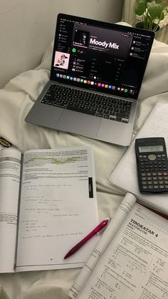 a laptop computer sitting on top of an open book next to a calculator