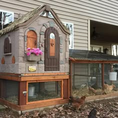 an outdoor chicken coop in front of a house with flowers on the window sill