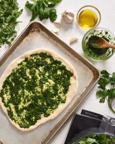 an uncooked pizza sitting on top of a pan next to herbs and olives