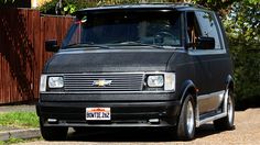 the black van is parked on the side of the road in front of a fence