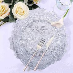 there is a glass plate with two forks on it and some flowers in the background