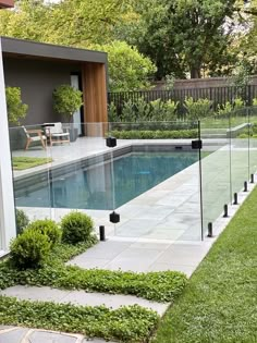 a glass fence around a pool in a backyard with grass and bushes on the side