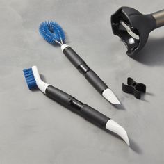 two toothbrushes, one blue and the other black with white tips are laying on a gray surface